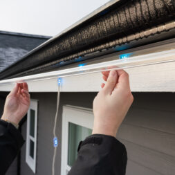 An installer puts up permanent outdoor lighting strips for a house