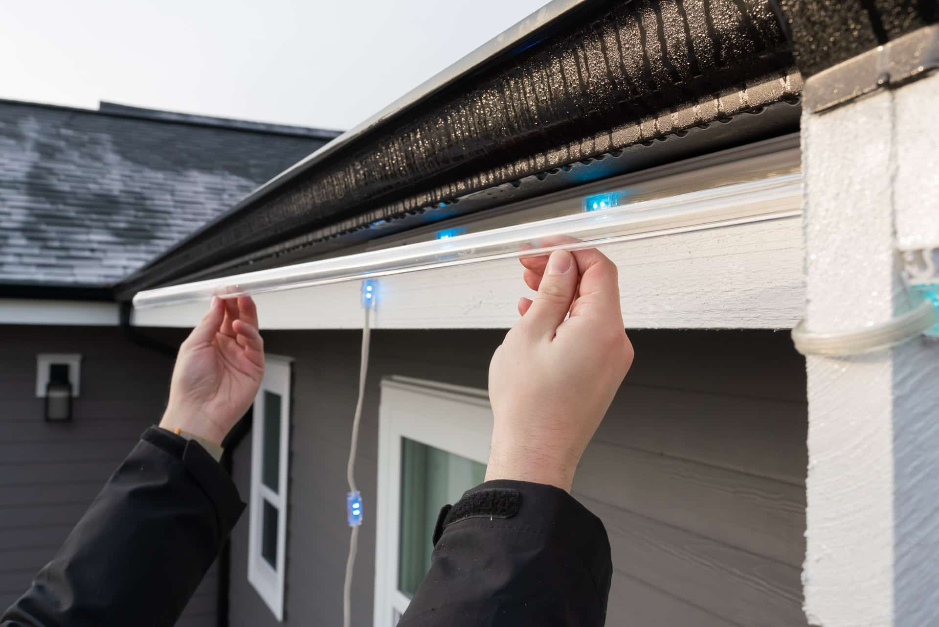 An installer puts up permanent outdoor lighting strips for a house
