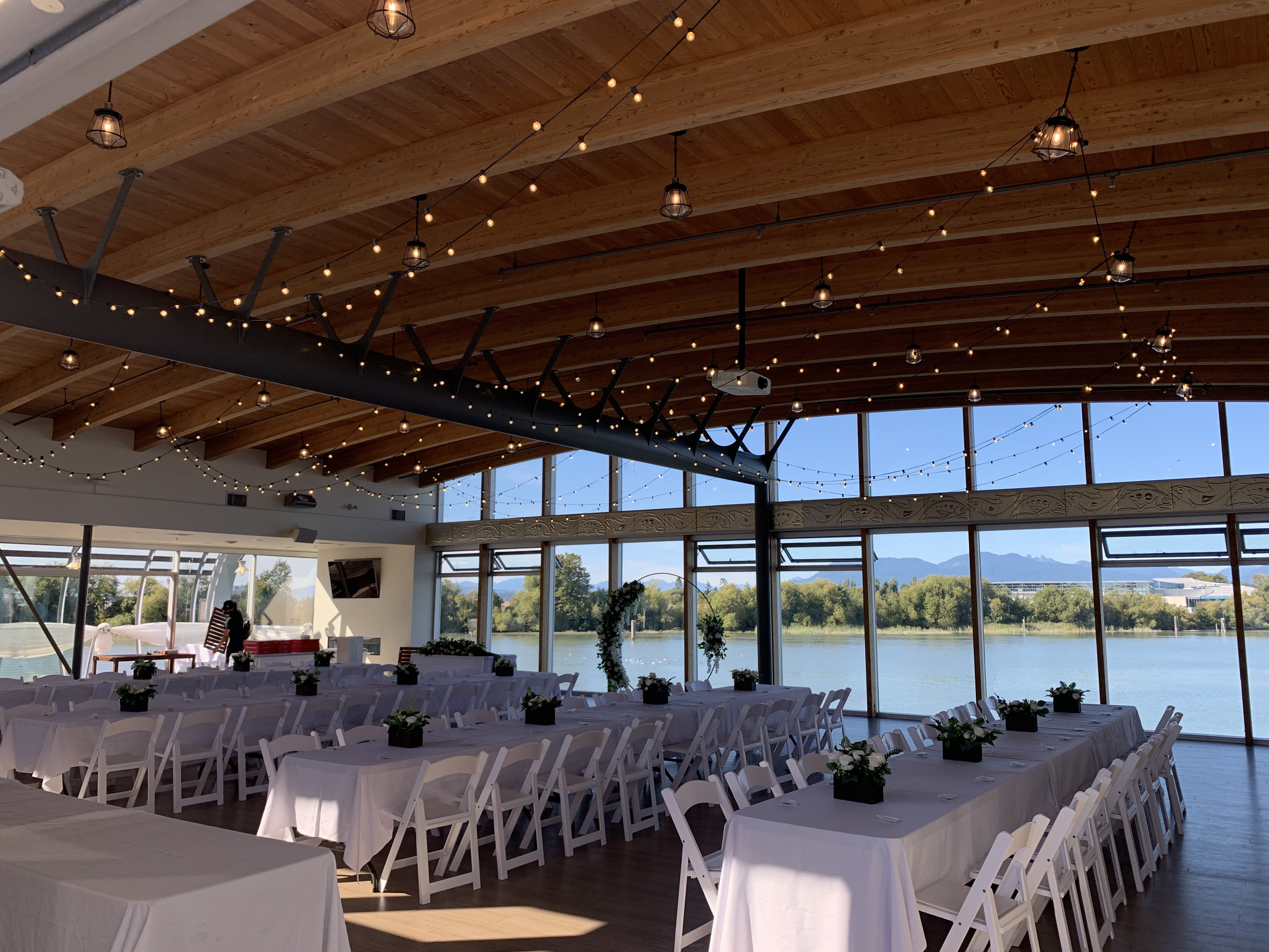 Wedding reception tables and charirs with decorations set up in building overlooking the water.
