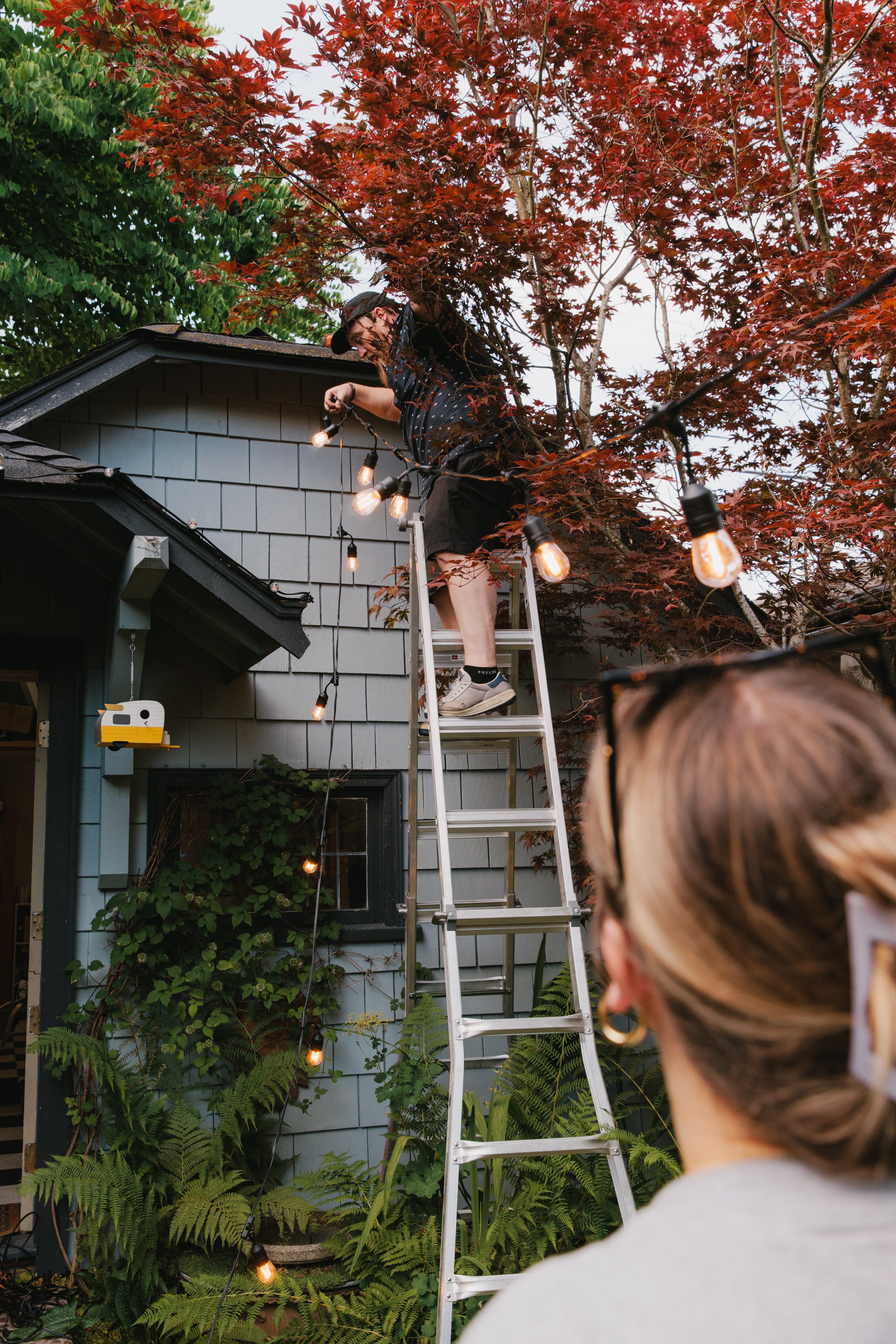 Patio lighting being installed by a custom lighting installer on tall ladder.