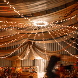 Canopy lights hang from lighting fixture with wedding decorations hanging from ceiling.