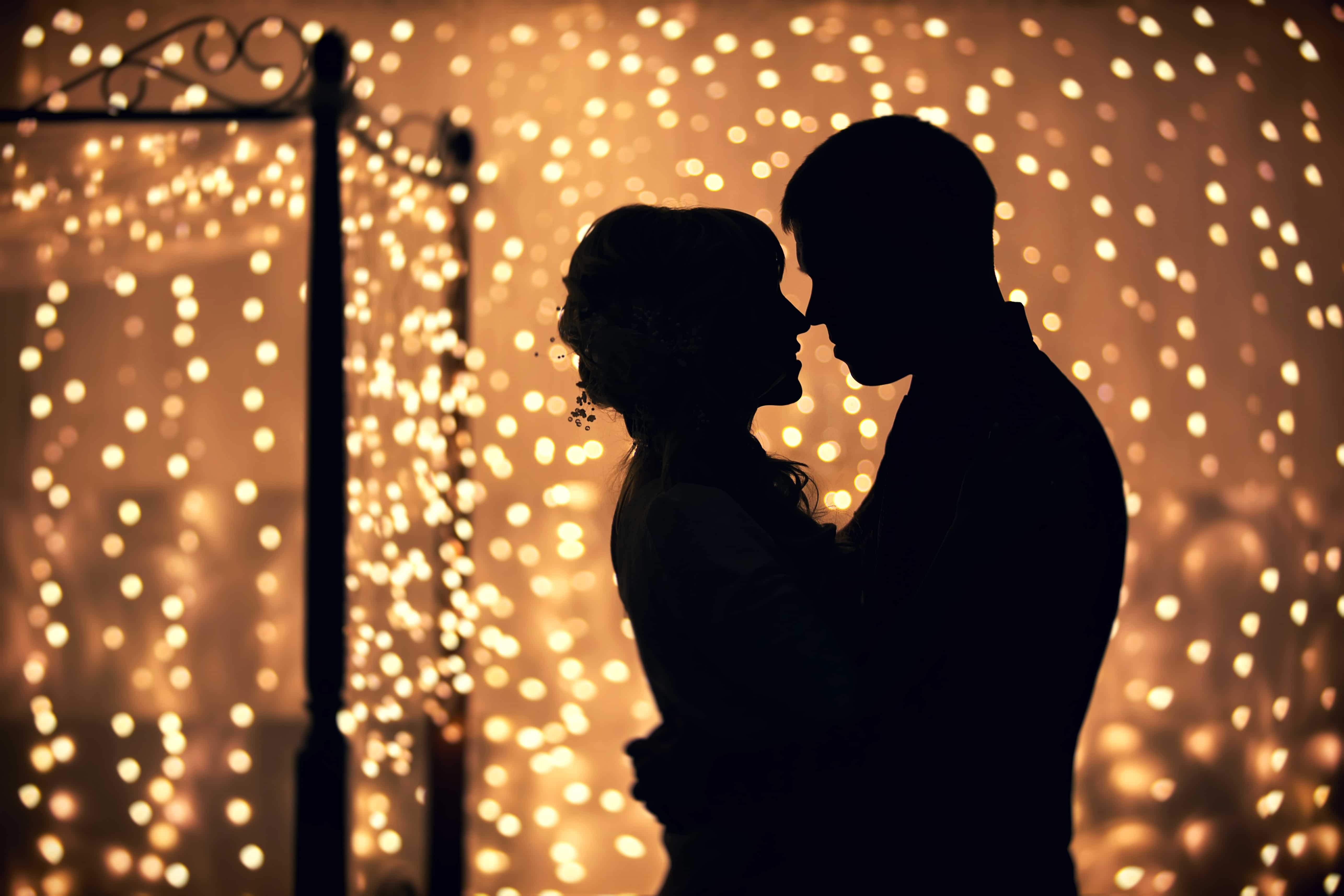 Silhouette of couple embracing with many small decorative lights glowing as the backdrop.